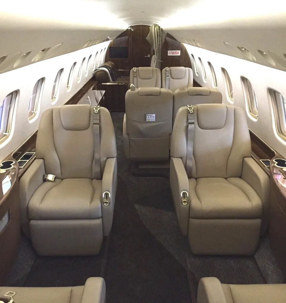 A view down the aisle of a private jet cabin, showing multiple rows of comfortable beige leather seats.