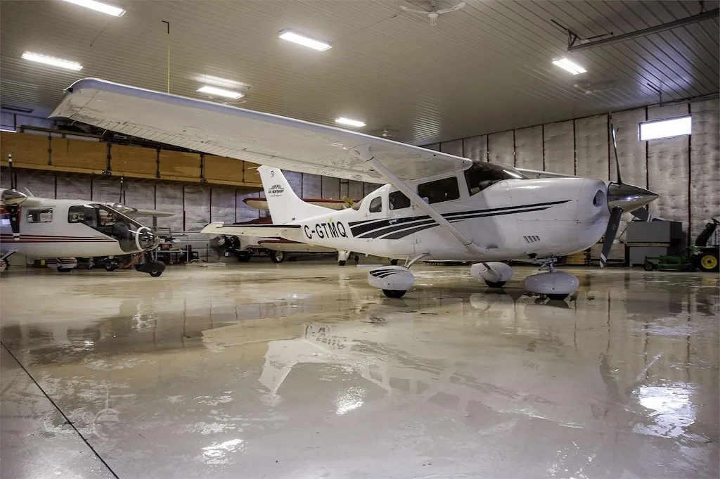 A white single-engine propeller aircraft, registration C-GTMQ, parked inside a brightly lit hangar with a reflective floor.