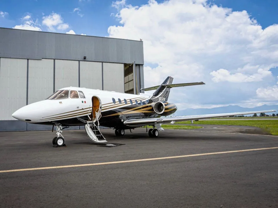 A private jet with a black, white, and gold paint scheme, registration XB-FLF, parked on an airfield with its passenger door open.