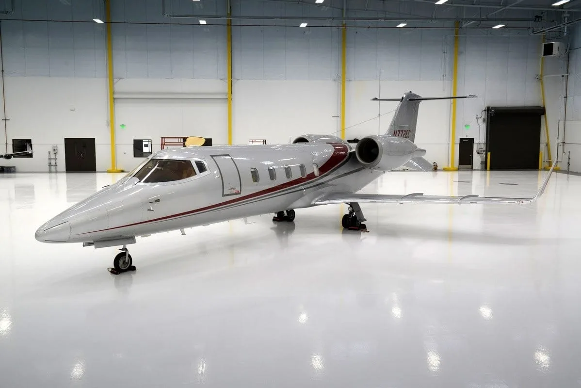 A silver business jet with a red stripe, tail number N772G, parked inside a brightly lit hangar.