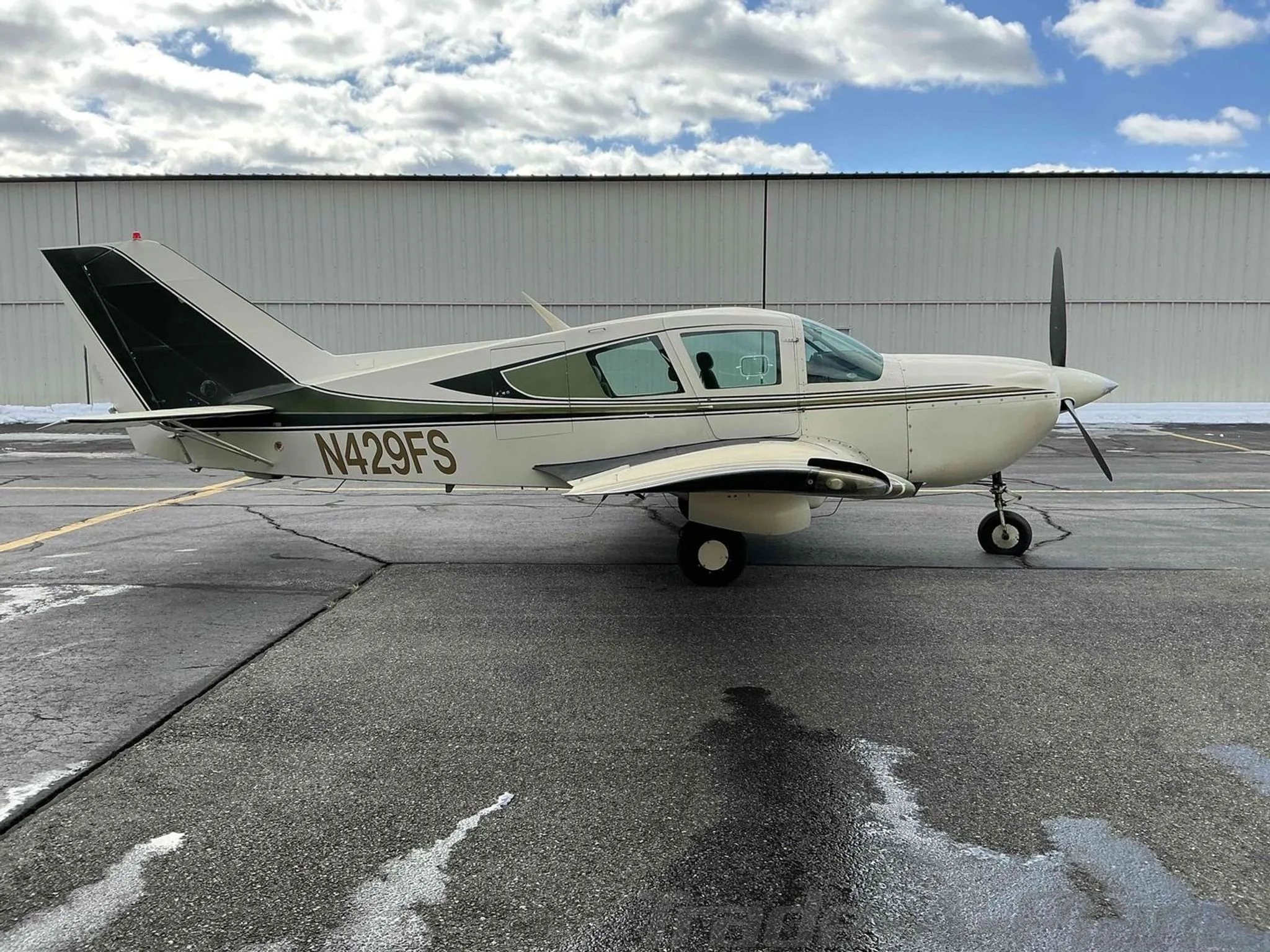 A side profile view of the white and green Bellanca Viking aircraft, N429FS, parked on an asphalt ramp.