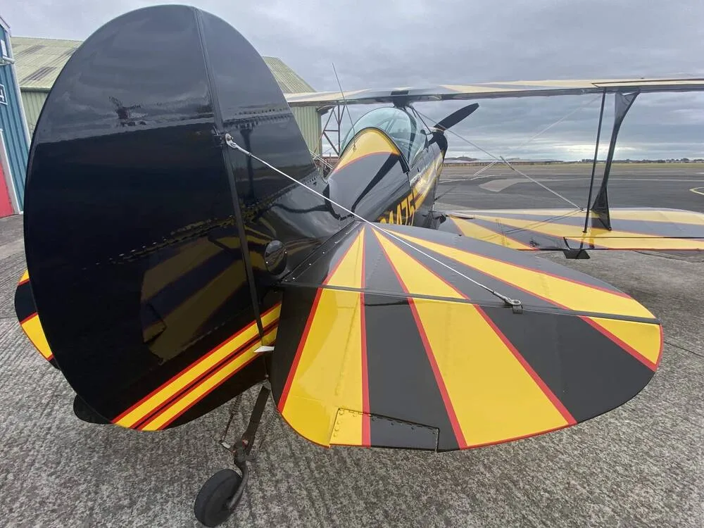 A close-up view of the black and yellow tail section of the biplane N31475 on an airfield.