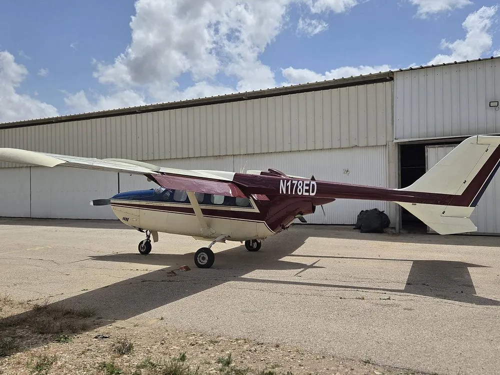 A cream, blue, and maroon Cessna 337 Skymaster with tail number N178ED parked next to a hangar.