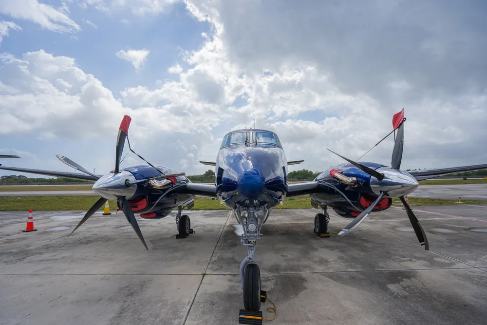 A front view of a blue and white twin-engine turboprop aircraft parked on a tarmac under a cloudy sky.