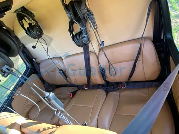 The rear interior of a helicopter shows tan leather seats with seatbelts and several headsets hanging from the ceiling.