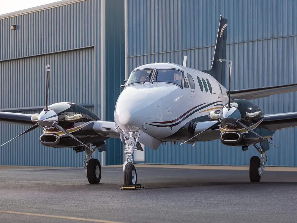 A front view of a white and black Beechcraft King Air aircraft with gold and red stripes parked on an tarmac.