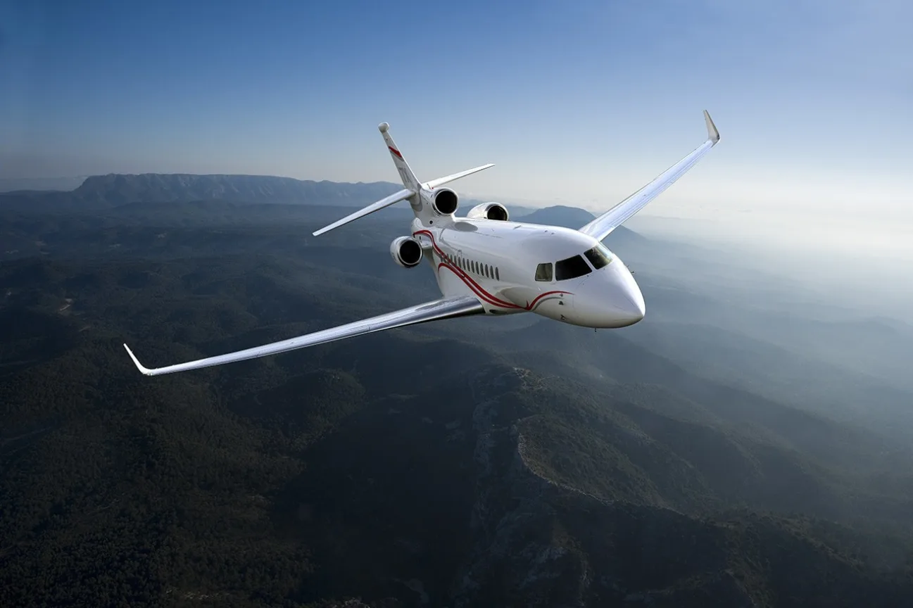 Front view of a white jet aircraft in flight over a mountainous landscape.