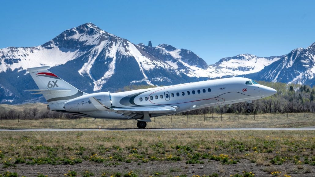 A Falcon 6X taking off with mountains in the background.
