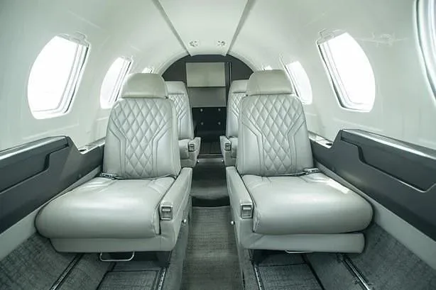 The aircraft's interior cabin shows two rows of light grey quilted leather seats facing each other.