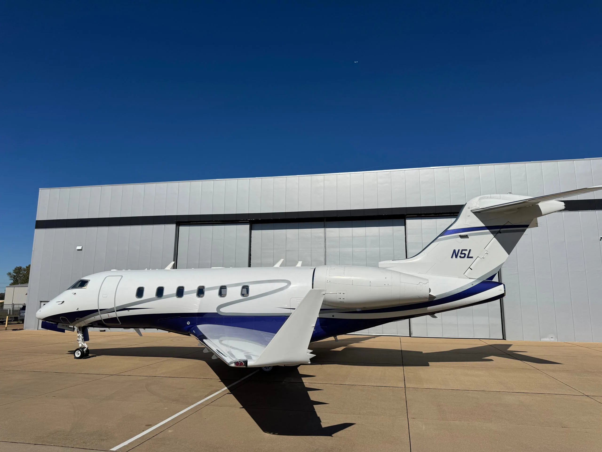 Side profile of the N5L business jet, a white aircraft with blue and silver stripes, parked on an airfield.