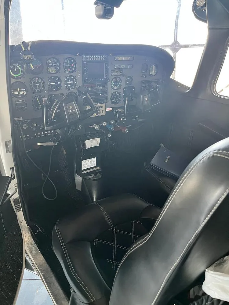 The cockpit of a Cessna aircraft shows the instrument panel and a black leather pilot's seat.
