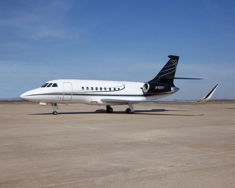 A white Dassault Falcon 900EX business jet with black tail and registration N48RR parked on an airport tarmac under a clear blue sky.
