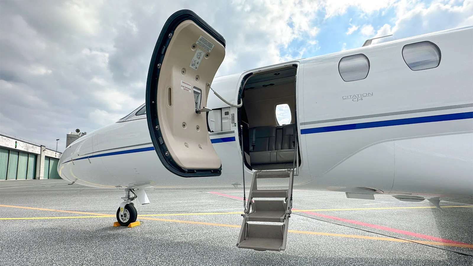 The open main cabin door and deployed airstairs of a white Cessna Citation CJ4 on the tarmac.