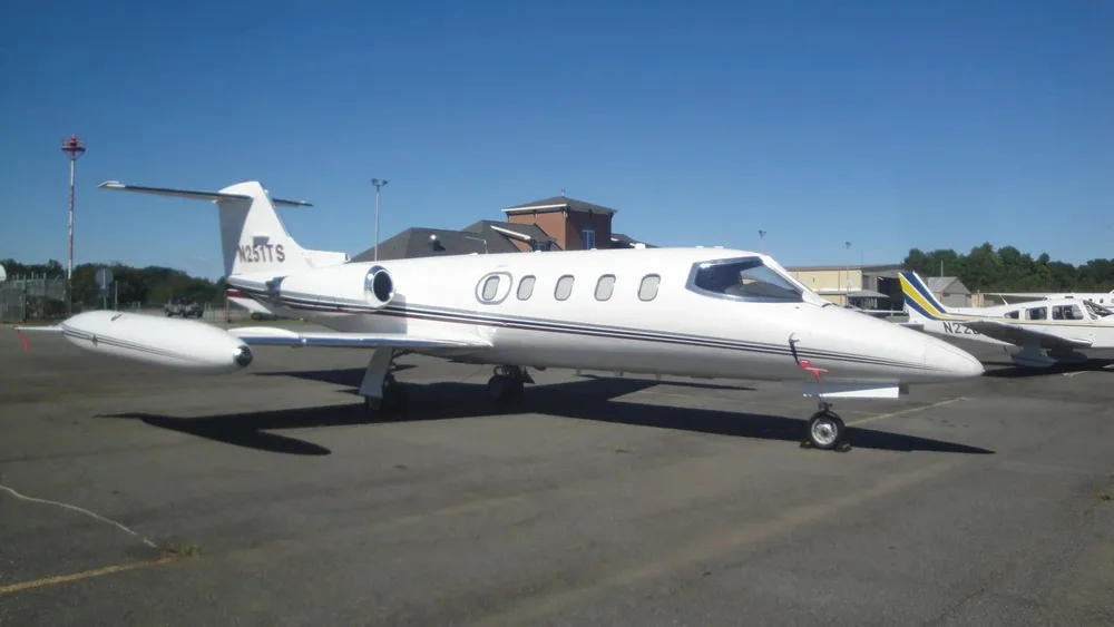 A white Learjet N251TS is parked on an airport tarmac, viewed from the front-left side.