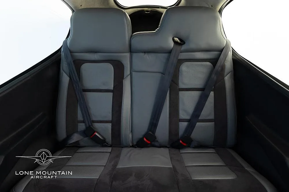 The grey leather rear seats of an aircraft cabin, with seatbelts.