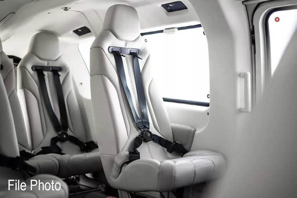 The interior of a helicopter cabin shows light gray passenger seats with black seatbelts.