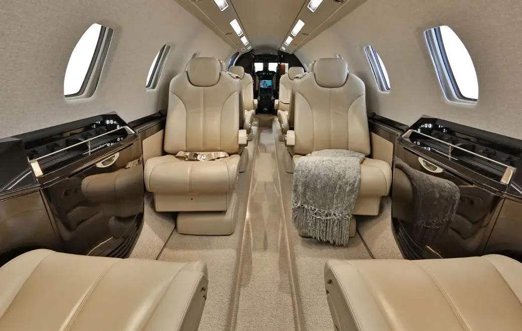 The luxurious cabin interior of a business jet, featuring tan leather seats and a gray blanket on one seat.