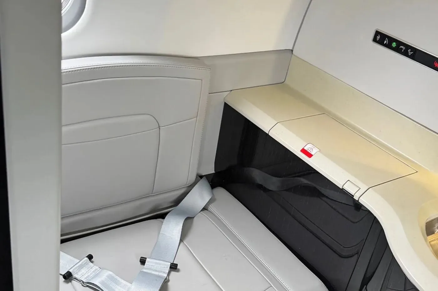 A close-up view of a light grey seat and a side panel with a small sink or counter in an aircraft interior.
