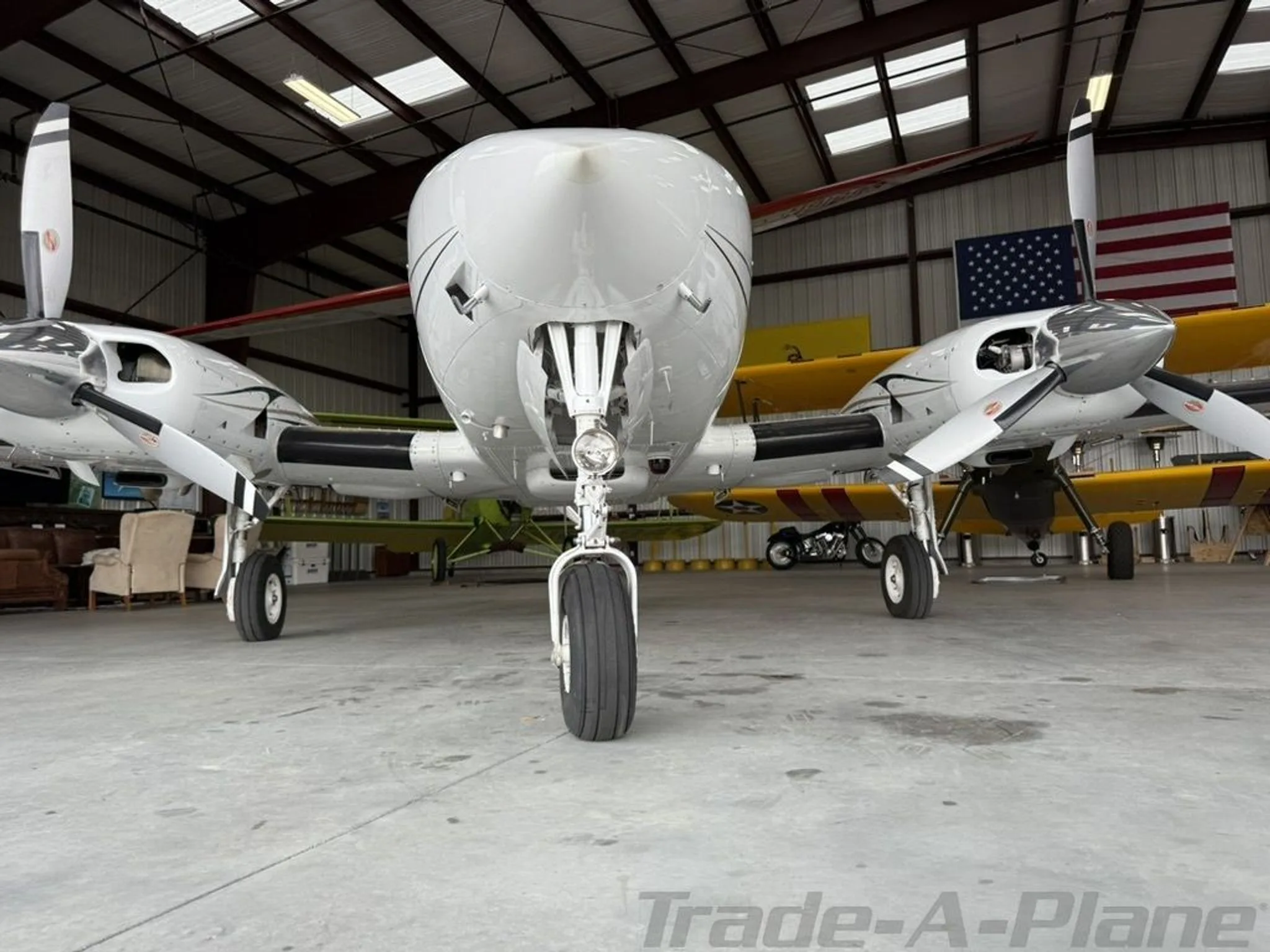 A front view of a white twin-engine aircraft, N653JR, parked inside a hangar with other aircraft in the background.