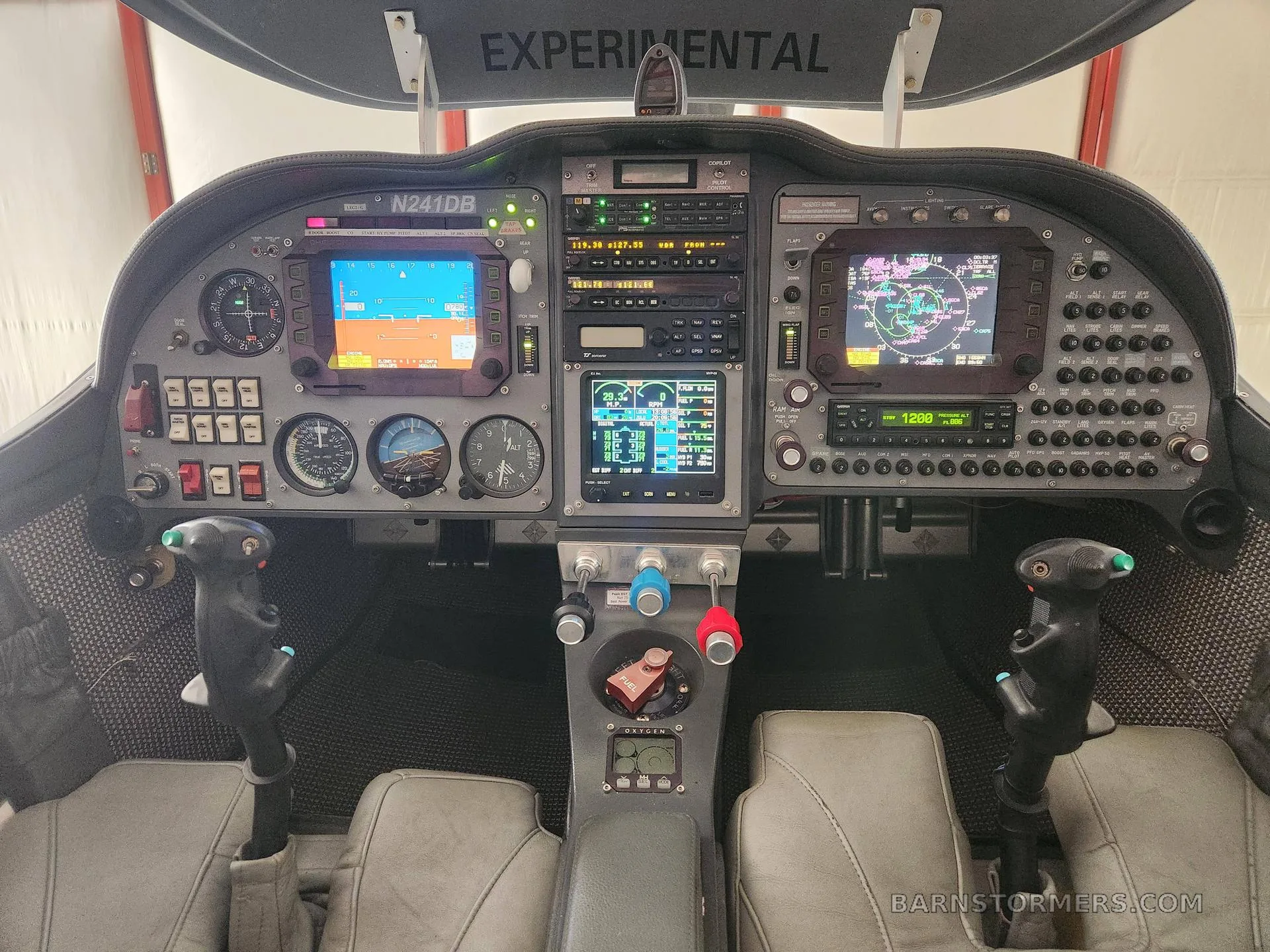 The cockpit of an experimental aircraft with multiple digital displays, analog gauges, and dual control sticks.