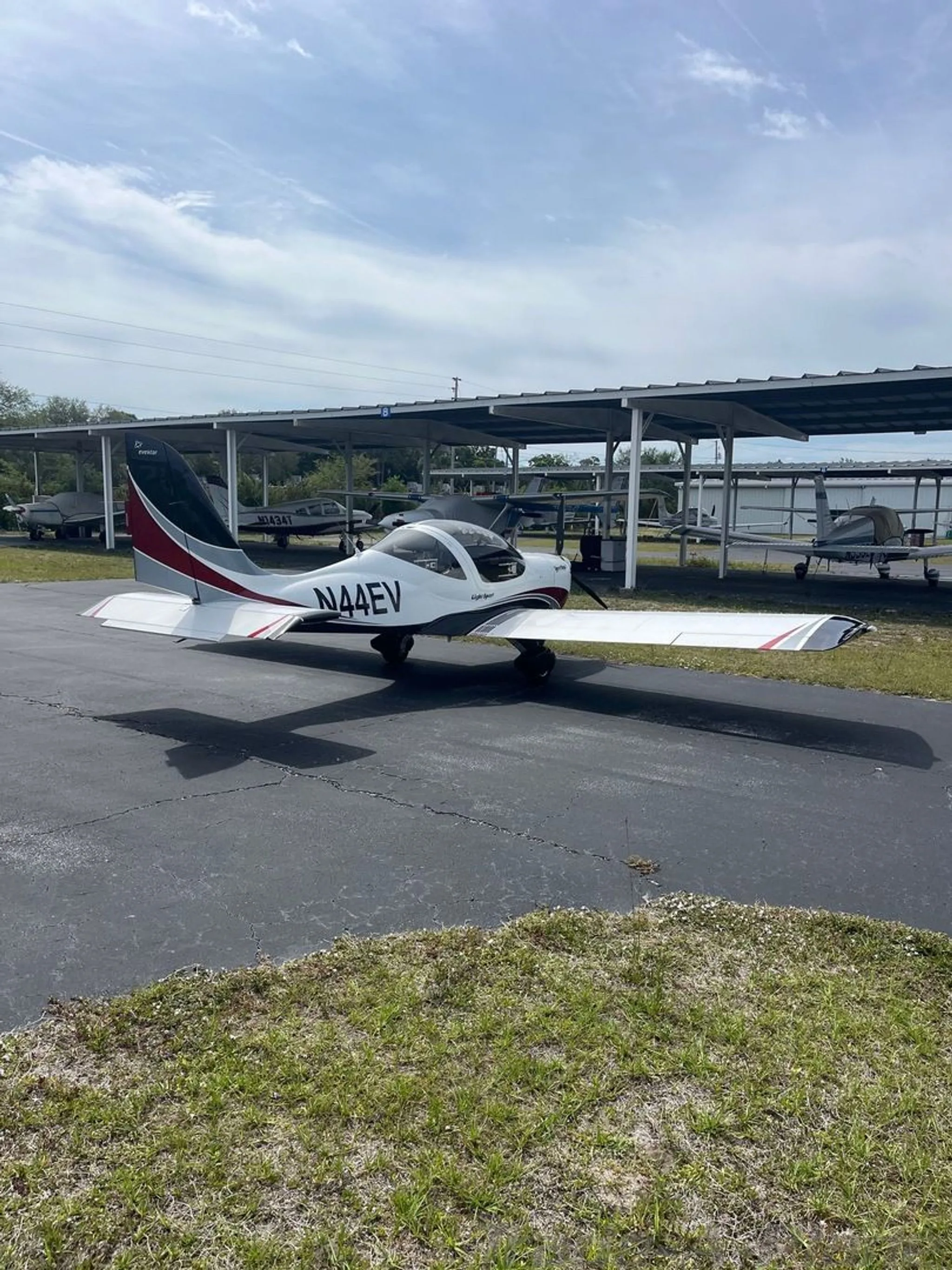 A three-quarter rear view of the white and red Evektor SportStar aircraft, tail number N44EV, parked on an asphalt ramp.