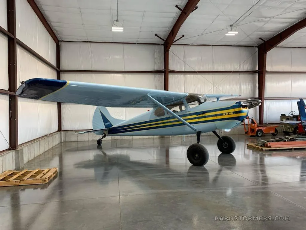 A light blue and yellow striped taildragger aircraft is parked inside a hangar.