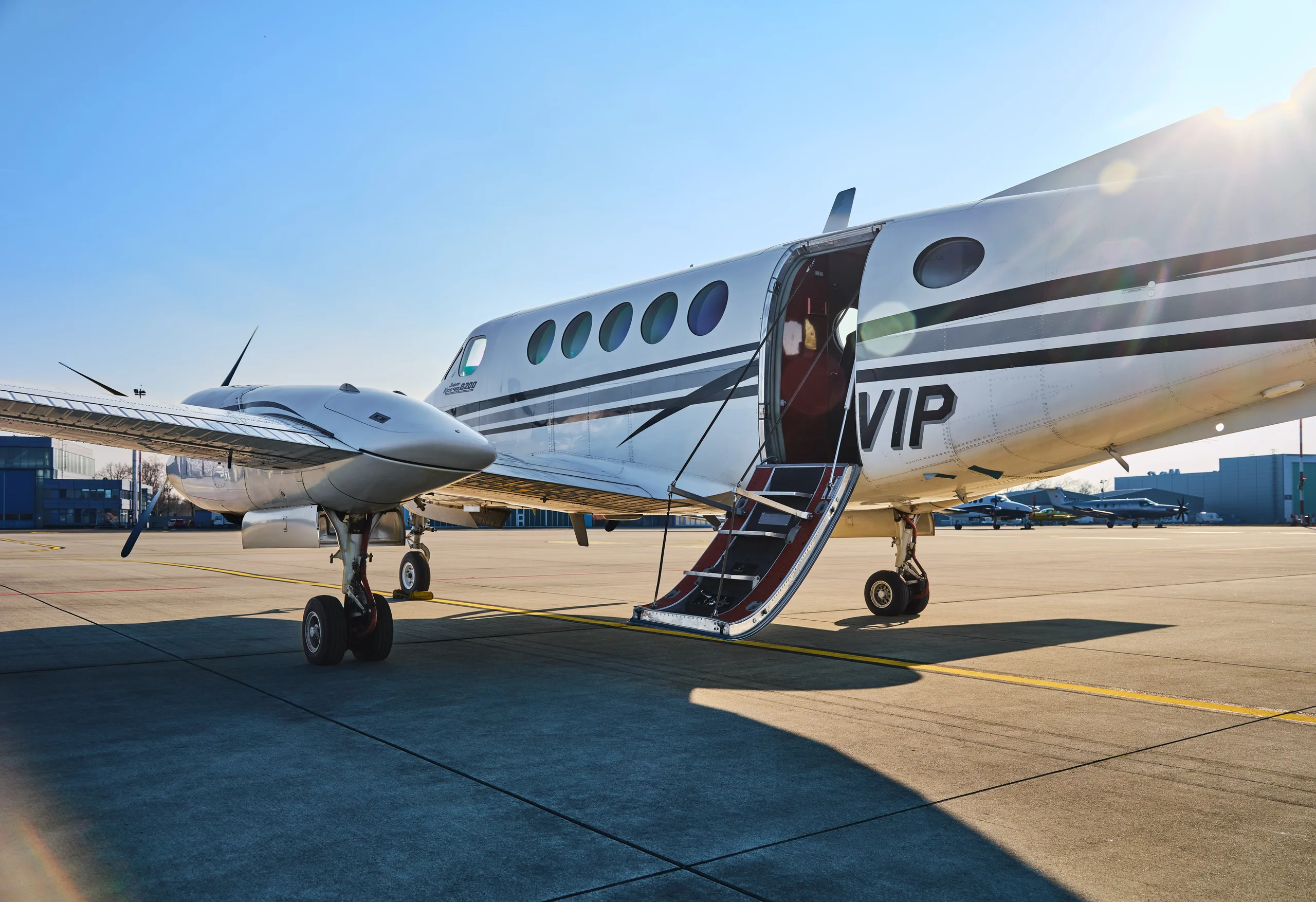 A white and black twin-turboprop aircraft, likely a King Air, is parked on an airfield with its passenger door open and stairs extended.