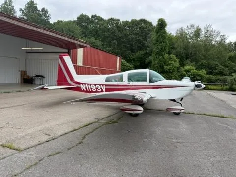 A white and red single-engine aircraft, N1193V, parked on an asphalt apron next to a hangar.