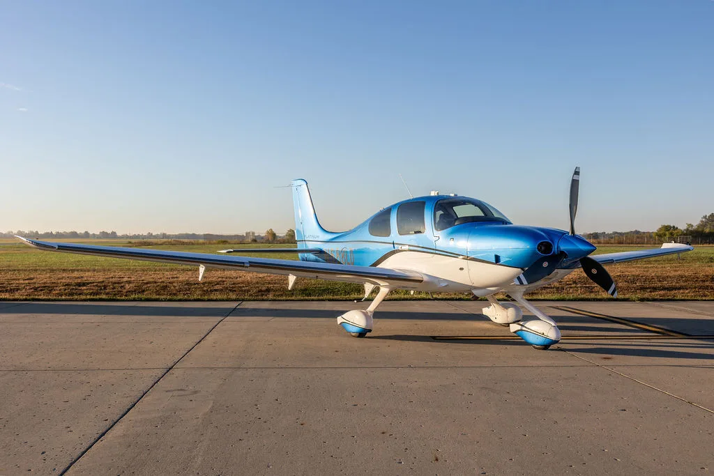 A blue and white Cirrus SR22 aircraft parked on an airfield with a clear sky.