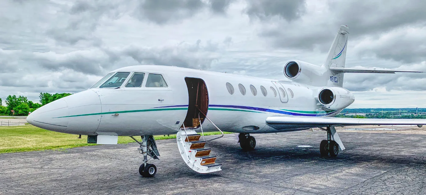 A Falcon 2000 aircraft with an open door and airstair on the tarmac.