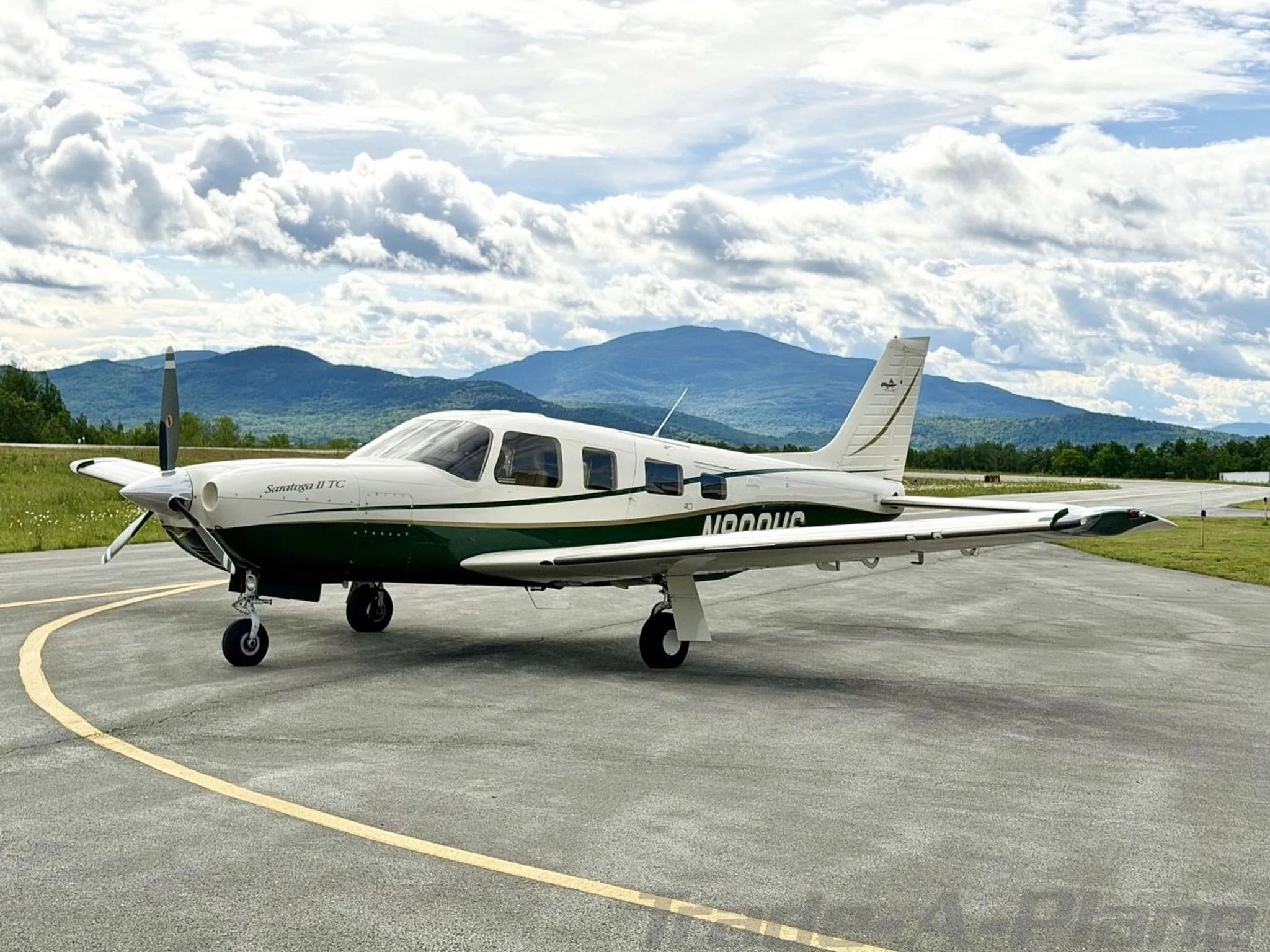 A white and green Piper Saratoga II TC aircraft, registration N800HS, parked on an asphalt ramp with distant mountains under a partly cloudy sky.