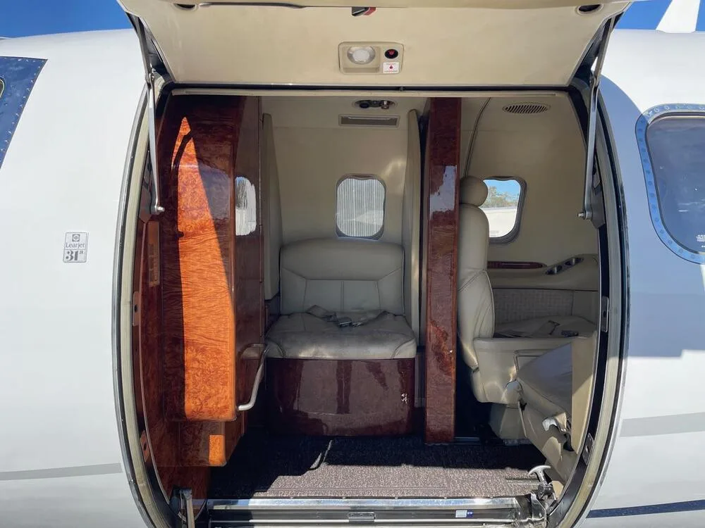 The open main entry door of the aircraft, revealing the interior cabin with beige seats and wood paneling.