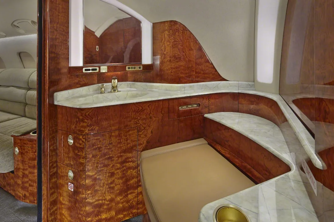 A luxurious aircraft lavatory with a marble countertop, sink, and rich wood paneling.