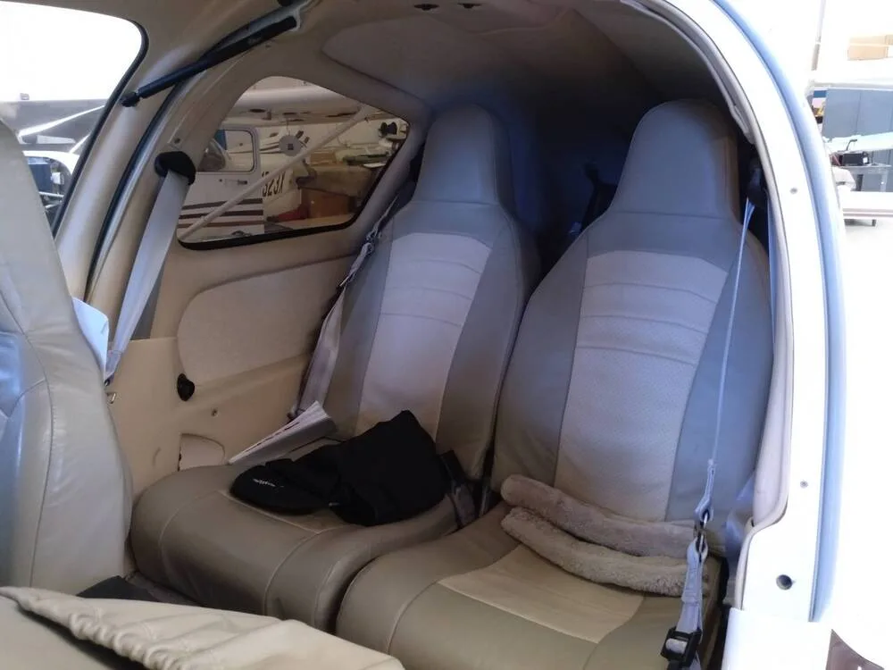 The tan leather rear seats of an aircraft cabin, with a black bag and blanket on them.