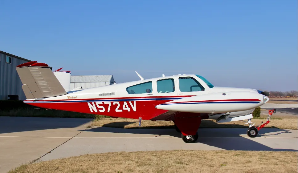 A side view of a red and white Beechcraft Bonanza N5724V parked on an airfield.