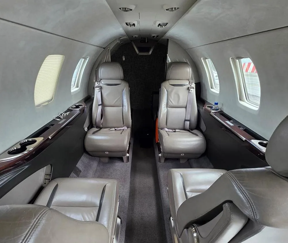 The interior cabin of a private jet, showing two rows of tan leather seats facing each other.
