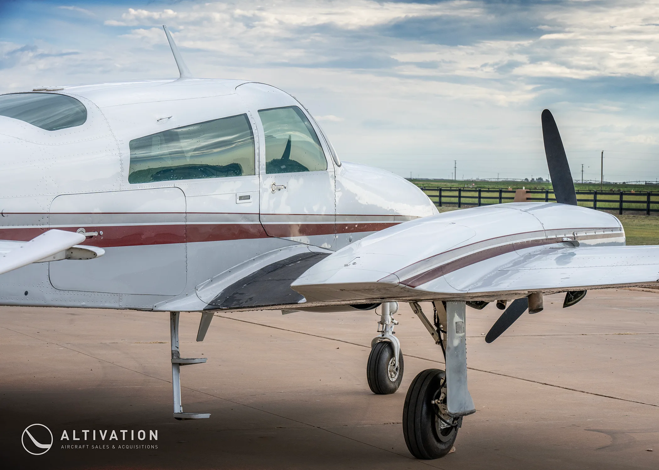 A close-up side view of the cockpit and wing of a white twin-engine propeller aircraft with red and grey stripes.