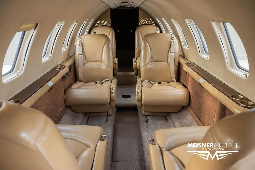 The interior cabin of a private jet with tan leather seats, viewed from the rear looking forward.