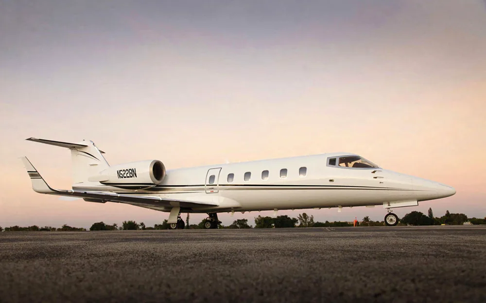 A white Learjet with black and grey stripes, tail number N522BN, parked on a tarmac at sunset.