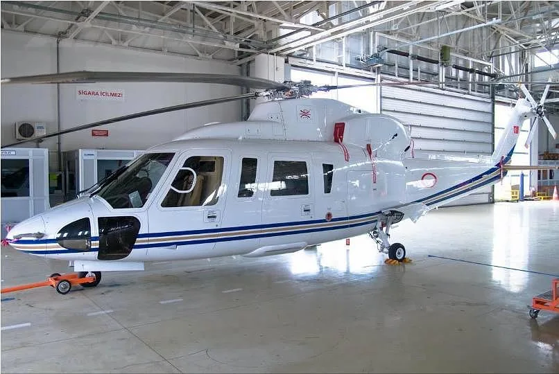 A white helicopter with blue and gold stripes is parked inside a hangar.