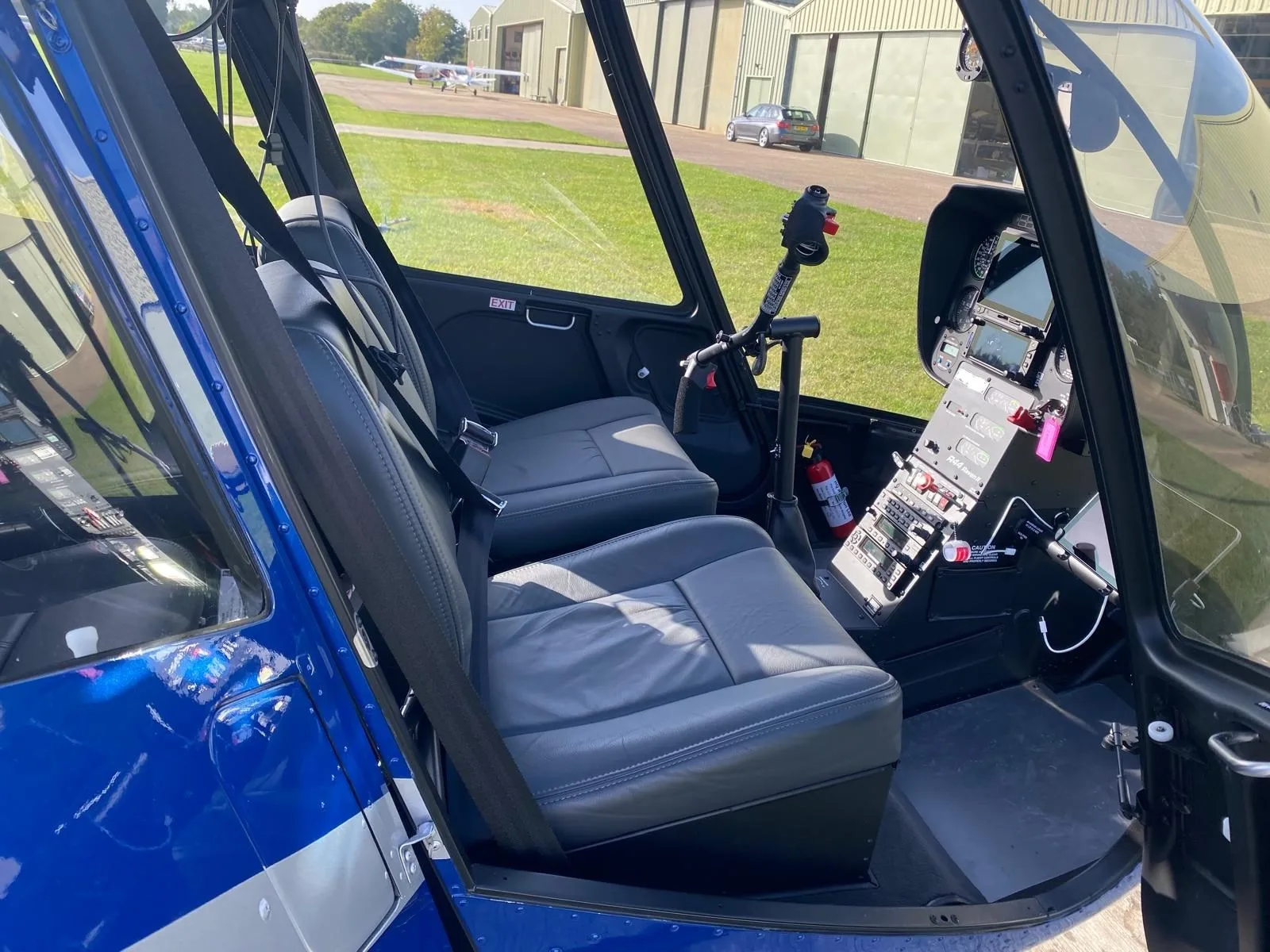 The grey leather interior seats and partial cockpit view of a blue Robinson R44 helicopter.