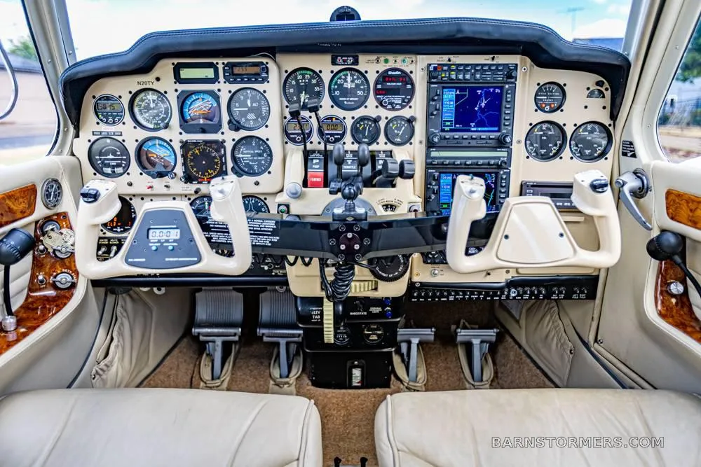 The cockpit of a twin-engine aircraft, showing a detailed instrument panel with analog gauges, two yokes, and modern avionics displays.