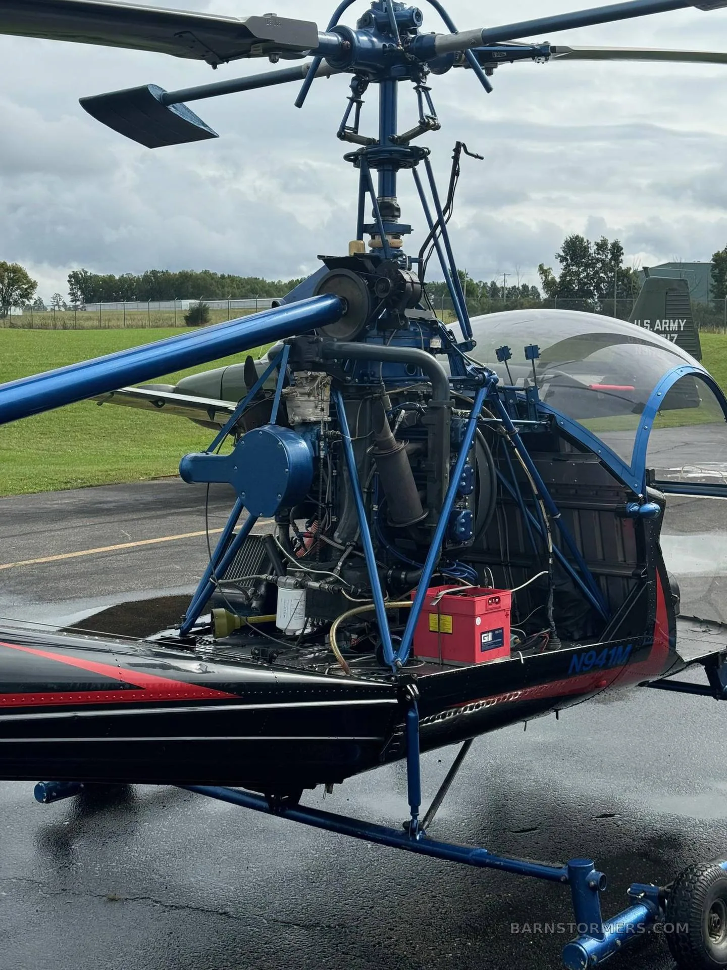 A close-up view of the exposed engine and rotor assembly of a blue and black helicopter on a wet tarmac.
