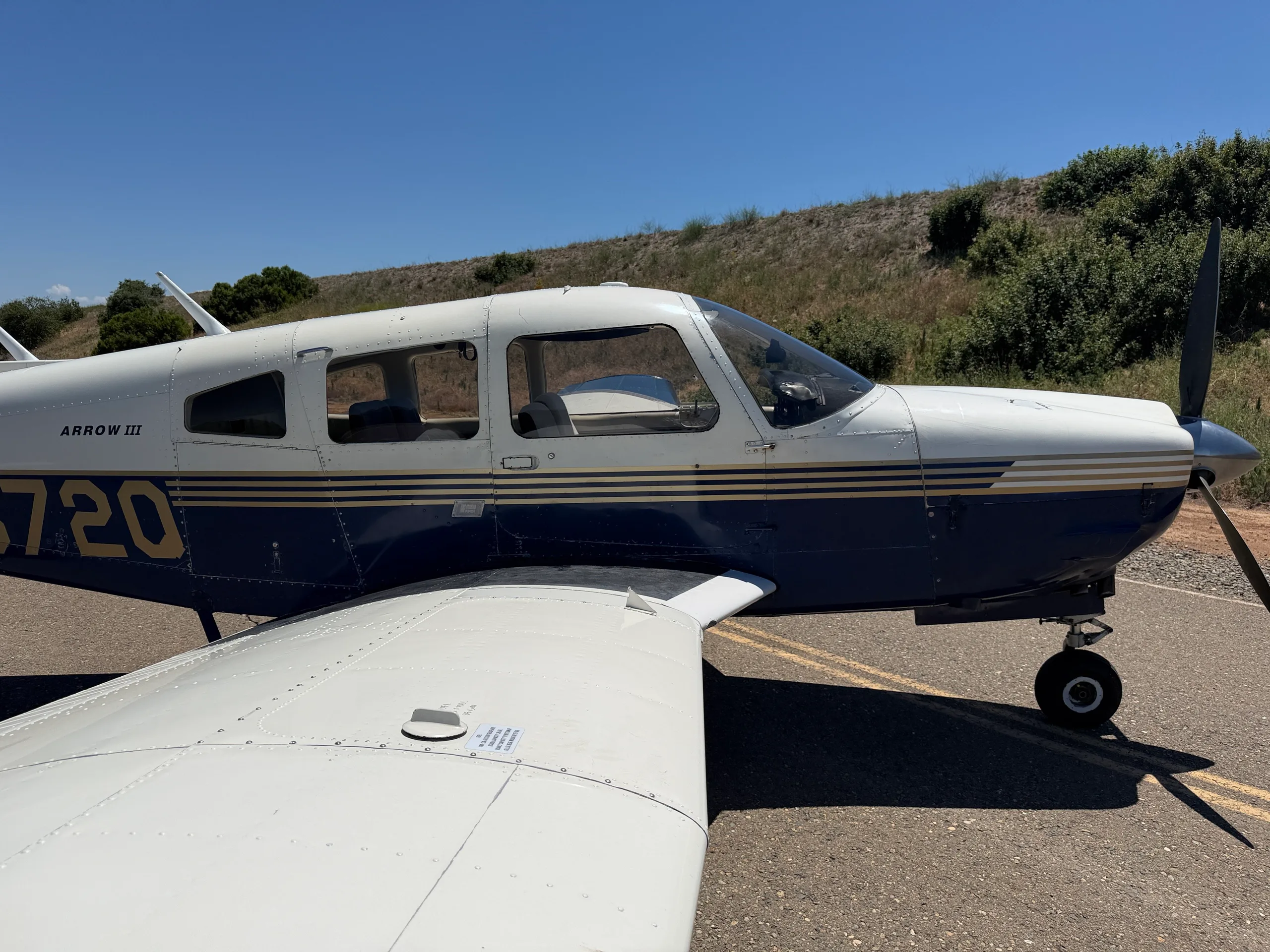 A side view of the white and blue Piper Arrow III aircraft, tail number N2672Q, showing the cockpit and wing.
