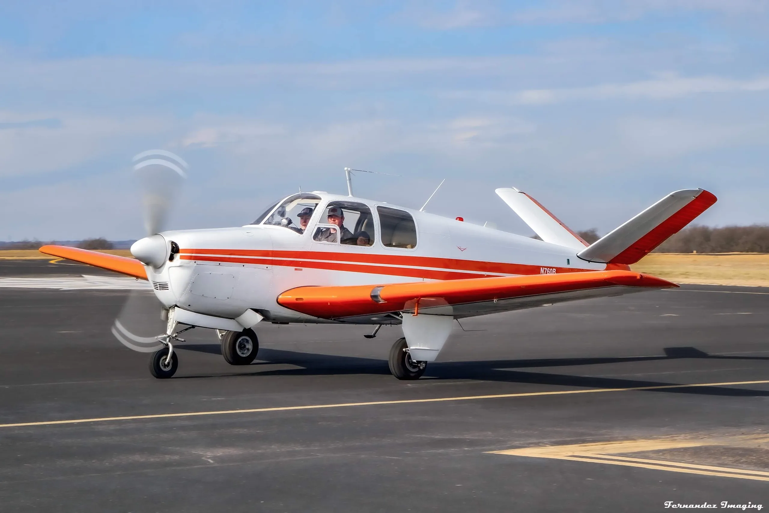 A white and orange single-engine aircraft, N760B, is taxiing on a runway with a pilot in the cockpit.