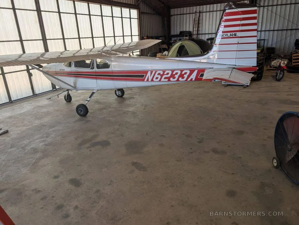 A white and red Cessna 182 Skylane (N6233A) parked inside a hangar, viewed from the rear-left.