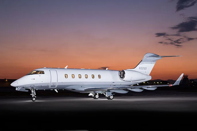 A white and grey Bombardier Challenger 3500 business jet is parked on a tarmac at sunset.