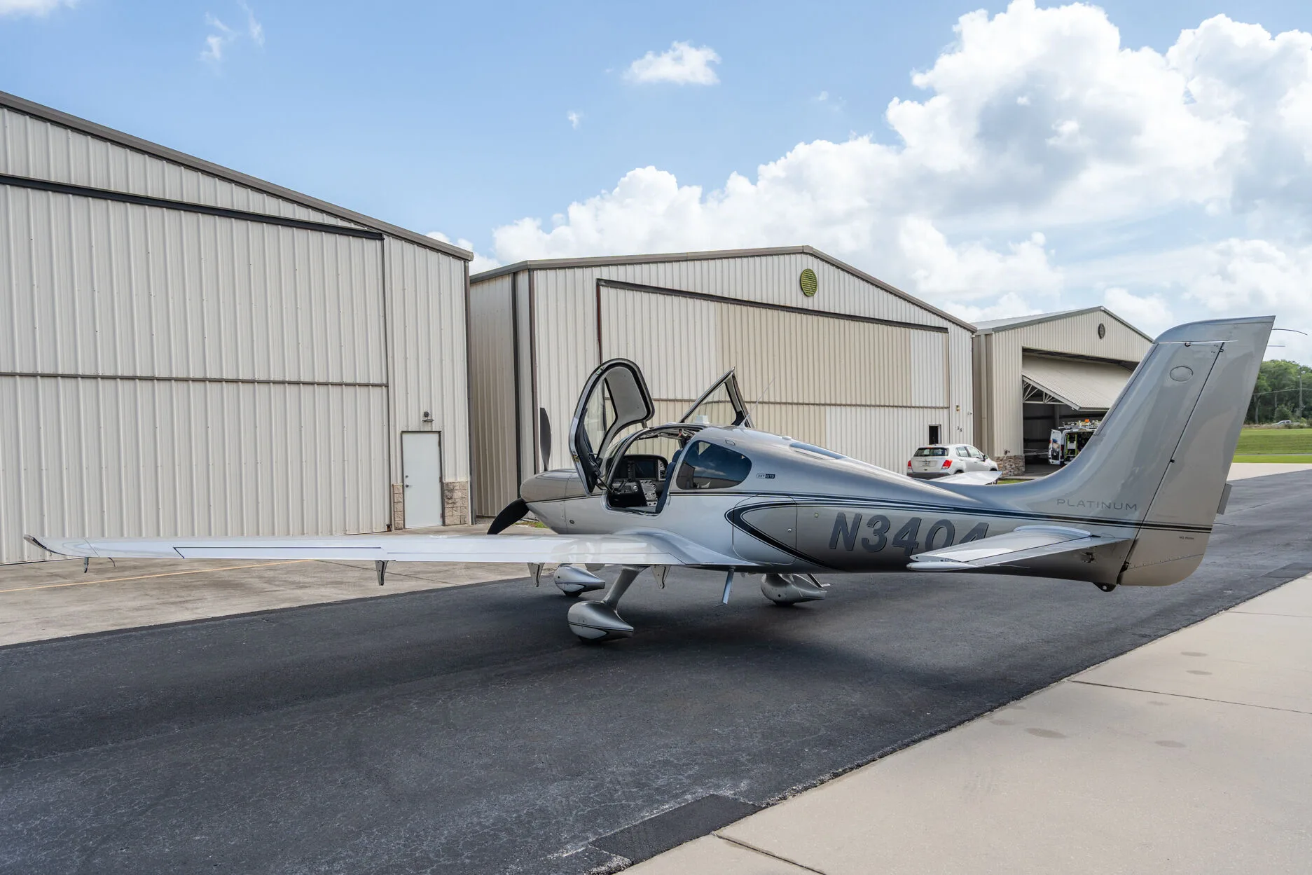 Three-quarter rear view of a silver Cirrus SR22T aircraft (N3404) with its gull-wing doors open, parked on an airport tarmac.