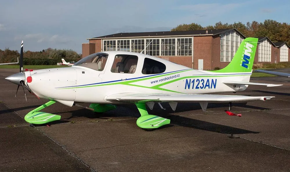 A white and green single-engine propeller aircraft, registration N123AN, parked on an asphalt apron with a building in the background.