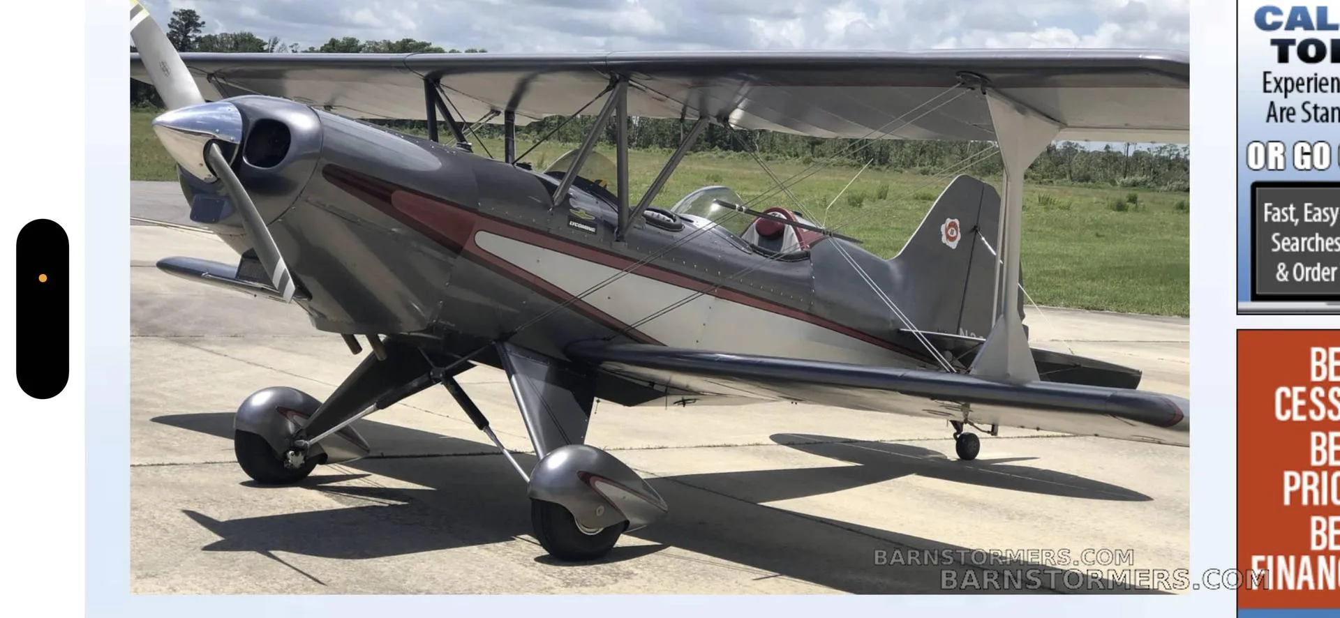A gray and white biplane with red accents is parked on an asphalt tarmac under a cloudy sky.